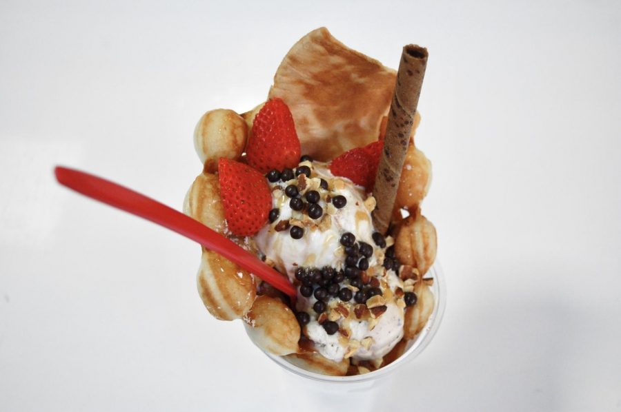 A bubble waffle drizzled with caramel syrup, strawberries, chocolate balls, and a chocolate stick.